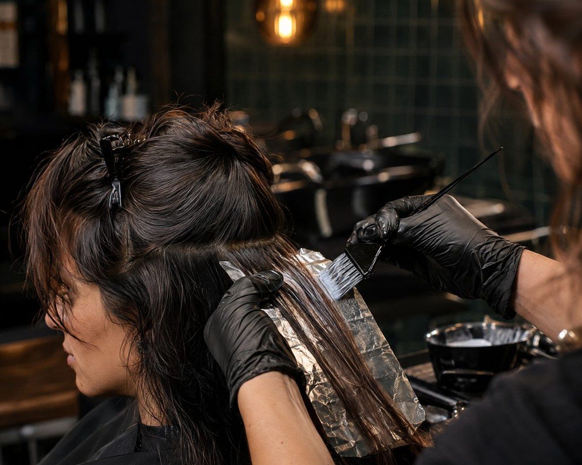 A colourist in black gloves applying colour with a tint brush to a foil section