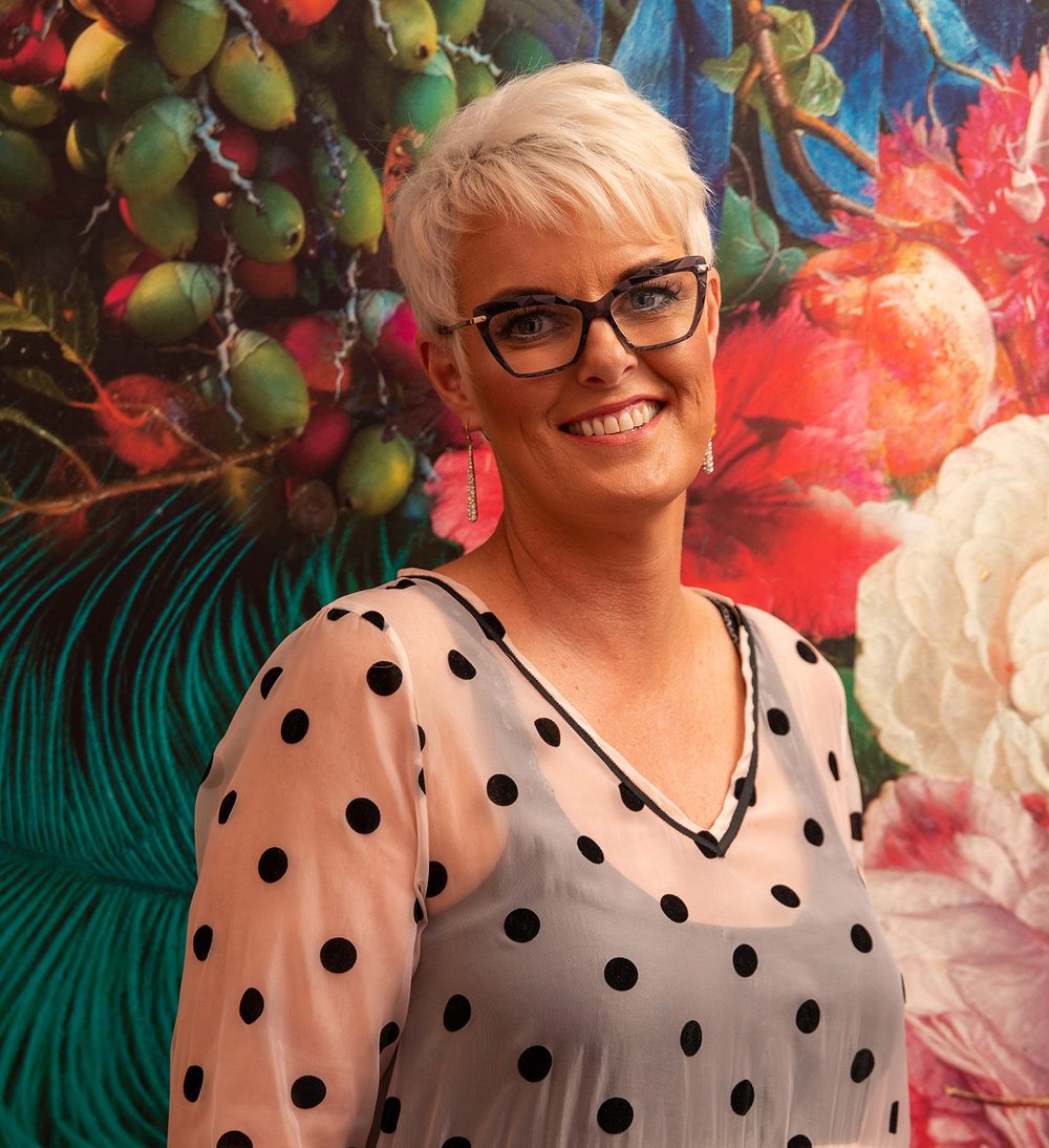 Vicki smiling in front of bold botanical wallpaper