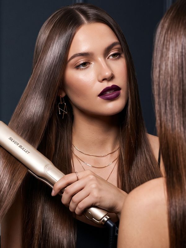 Woman with long sleek brunette hair using the Silver Bullet Asteria champagne hair straightener